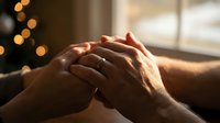 Elderly couple holding hands in warm sunlight with Christmas lights bokeh background showing love, care and togetherness during holiday season.