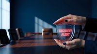 Young professional with medium skin tone holding glowing security alert shield in modern office conference room with dark blue background and wooden table.