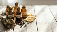 Natural essential oil bottles with dried herbs and citrus slices on rustic wooden background for aromatherapy and wellness treatments.