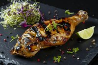 Grilled chicken leg with teriyaki glaze, fresh microgreens and lime on black slate. Gourmet food styling with Asian fusion flavors and garnish.