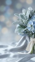 Soft blue hydrangea bouquet with dusty miller leaves tied with lace ribbon on white fabric background for wedding and romantic occasions.