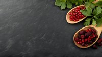 Fresh red currants and blackberries in wooden spoons with green parsley leaves on dark stone background, copy space for healthy food design.