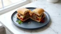 Freshly baked meatball sandwiches with melted cheese and marinara sauce served on a slate plate near a bright window for lunch or dinner.