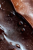 Melted dark chocolate surface with water droplets creating artistic texture and shine. Close-up macro photography shows rich brown tones and glossy reflections.