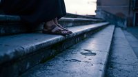Feet in leather sandals on wet stone steps at dusk, low angle view with moody blue tones and shallow depth of field.