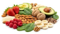 Healthy organic food collection with fresh fruits, nuts, seeds and leafy greens arranged on white background for nutritious diet and wellness lifestyle.