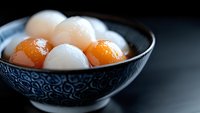 Traditional Asian dessert with white and orange glutinous rice balls in patterned ceramic bowl against dark background, selective focus on sweet dumplings.