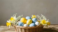 Easter basket with colorful eggs, daffodils and pussy willow branches on wooden table against neutral background for spring holiday celebration.