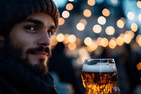 Man holding beer glass outdoors at night with bokeh lights in background, winter holiday celebration, beverage and lifestyle concept for seasonal advertising.