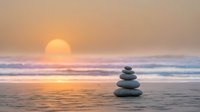 Zen stone stack on beach at sunset with golden sky and ocean waves creating peaceful meditation atmosphere for wellness and mindfulness practices.