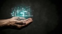 Male hand holding glowing digital cityscape with data visualization and financial charts, representing smart city technology, urban development, and business innovation on dark background.