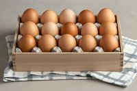Fresh brown chicken eggs arranged in wooden box with paper dividers on checkered kitchen towel, natural organic food concept for cooking and baking.