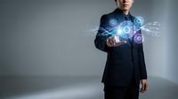 Professional businessman in dark suit interacting with futuristic holographic interface displaying glowing blue digital icons and network connections.