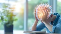 Young Asian man holding head in hands with glowing brain visualization overlay, depicting mental stress, anxiety and cognitive overload at desk.