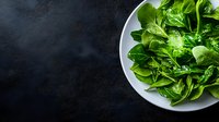 Fresh green butterhead lettuce leaves arranged on white ceramic plate against dark background, food photography for healthy eating and salad recipes.