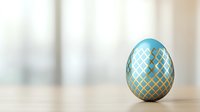 Decorative turquoise Easter egg with golden geometric pattern on wooden surface against light blurred background. Elegant holiday composition with copy space.