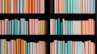 Colorful book spines arranged on dark wooden shelves creating abstract pattern in pastel pink, mint green, and peach tones. Modern minimalist library interior.