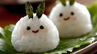 Cute Japanese rice balls onigiri with smiling faces and nori seaweed details arranged on green leaf. Traditional Asian food styling with kawaii character design.