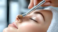 Young Caucasian woman receiving professional makeup application with brush on nose area during beauty treatment at spa salon, closeup of relaxed face with closed eyes.