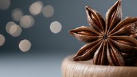 Star anise spice on wooden surface against blurred bokeh background, aromatic brown dried flower-shaped pod in macro photography, culinary ingredient.