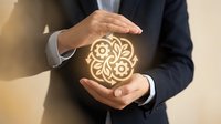 Businessman in dark suit holding glowing gear and flower symbol between hands, representing innovation, creativity, and business growth strategy.