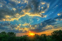 Dramatic sunset sky with vibrant sunbeams breaking through golden clouds over green forest silhouette, creating magical atmospheric scenery for nature and landscape photography.