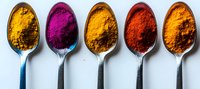 Vibrant colorful spices in silver spoons arranged in row showing yellow turmeric, pink beetroot, curry, red paprika and saffron powders on white background. For food and cooking design.