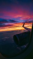 Airplane wing silhouette against dramatic sunset sky with vibrant pink, orange, and purple clouds during flight, aerial travel photography.