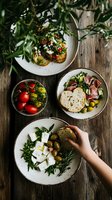 Mediterranean appetizer plates with fresh feta, olives, prosciutto, cherry tomatoes and artisan bread served on rustic ceramic dishes on wooden table. Overhead view.