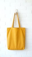 Yellow canvas tote bag hanging on white brick wall hook for eco-friendly shopping and sustainable lifestyle choices.