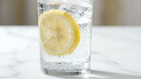 Refreshing glass of sparkling water with fresh lemon slice and ice cubes on marble surface, perfect for beverage, food and drink, wellness and hydration concepts.