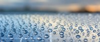 Water droplets on blue metallic surface with shallow depth of field creating bokeh background for automotive and industrial design concepts.