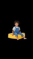 Toddler boy with curly dark hair and medium skin tone sitting on yellow foam block, wearing blue overalls and striped shirt, isolated on transparent background for design use.