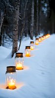 Glowing mason jars with candles create magical path lighting through snowy winter forest, illuminating dark evening with warm amber light against white snow and birch trees.
