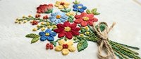 Colorful floral embroidery bouquet with red, blue and yellow flowers on white fabric. Traditional needlework craft design for home decor and textile projects.