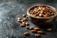 Fresh roasted almonds in rustic wooden bowl on dark textured background with scattered nuts and copy space. Food photography for healthy snacks.