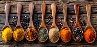 Colorful aromatic spices and herbs in wooden spoons on rustic background with peppercorns, turmeric, paprika, curry powder arranged in line. Food seasoning concept.