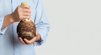 Caucasian male in light blue shirt holding fresh brown coconut with stem, isolated on white background for food and beverage marketing.