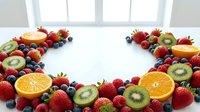 Fresh mixed berries and citrus fruits arranged in heart shape on white background for healthy eating and nutrition concepts.