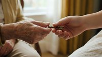 Elderly woman receiving medication pills from caregiver hand in bright home setting showing healthcare assistance and senior care support.