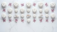 White meringue cookies and purple flower petals arranged in neat rows on marble surface for baking and dessert photography.