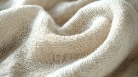 Natural linen fabric with soft folds and texture in beige color showing detailed weave pattern and gentle waves in macro photography.