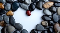 Smooth river stones arranged in heart shape with single red stone accent on white background, creating zen-like composition for wellness and spa designs.