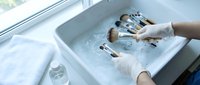 Medical professional sterilizing dental instruments in ultrasonic cleaning bath wearing protective gloves in modern clinic environment.
