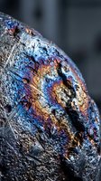 Iridescent mineral specimen displaying rainbow metallic colors and crystalline formations on weathered rock surface for geology and earth science applications.