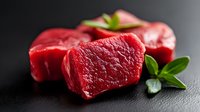 Fresh raw beef tenderloin pieces with green herbs on black stone background, close up view of juicy red meat cuts for restaurant menu or cooking.