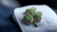Handcrafted green shamrock embroidery pin on white fabric against blue background, symbolizing Irish heritage and luck for St. Patrick's Day celebrations.