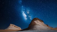Majestic sandstone rock formations in desert landscape against vibrant night sky with bright Milky Way galaxy and countless stars illuminating dark blue space.