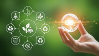 Hand holding glowing light bulb with renewable energy icons on green background representing sustainable technology and environmental solutions.
