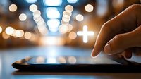 Digital healthcare concept with glowing medical cross on tablet screen against blurred bokeh lights background, finger touching interactive display.
